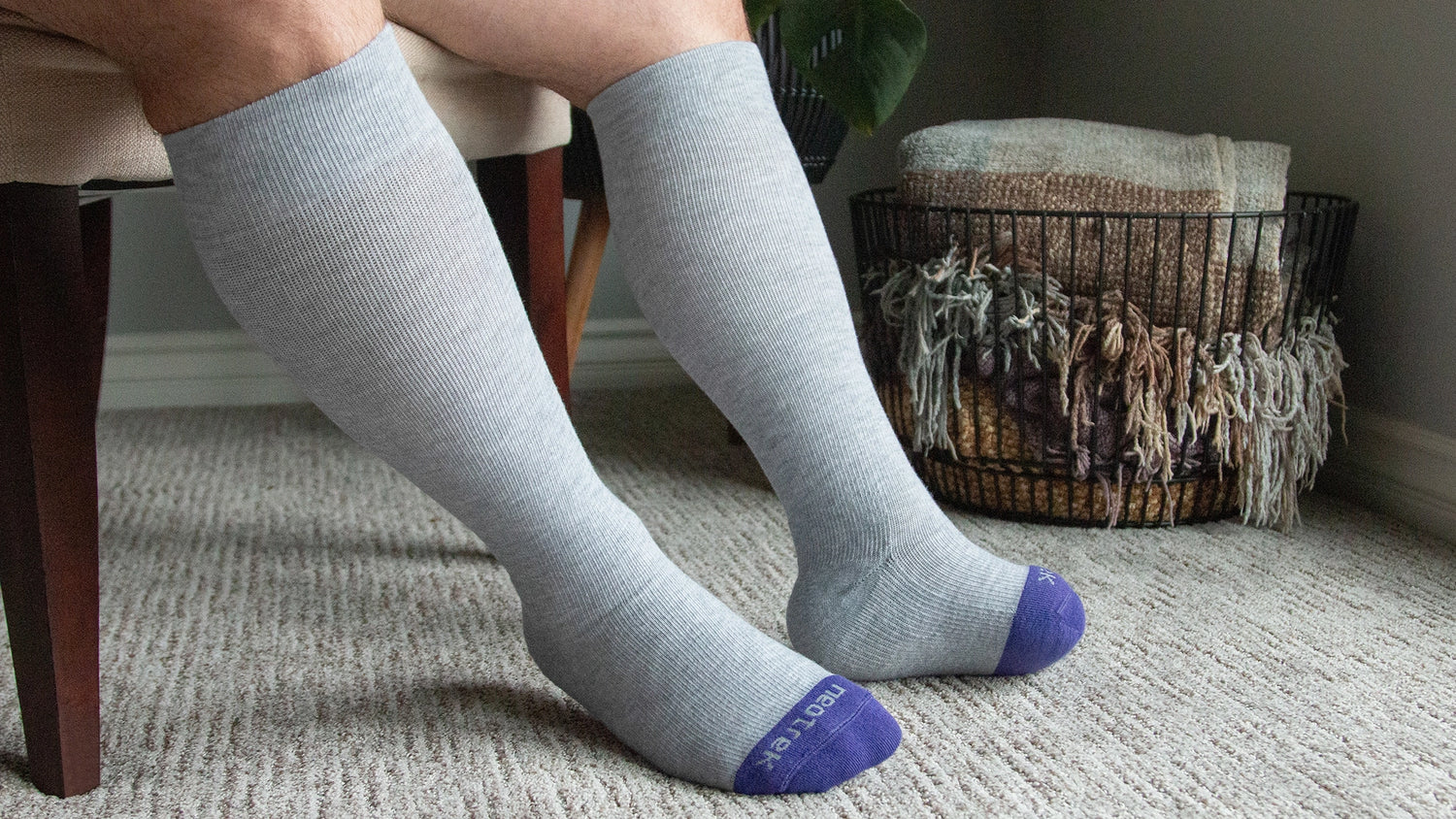 Person wearing light gray knee-high socks with purple toes and heels on a carpeted floor.